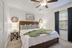 Ein Schlafzimmer mit einem hölzernen Bett, zwei Nachttischlampen, einem Deckenventilator und einem Fenster mit Jalousien.