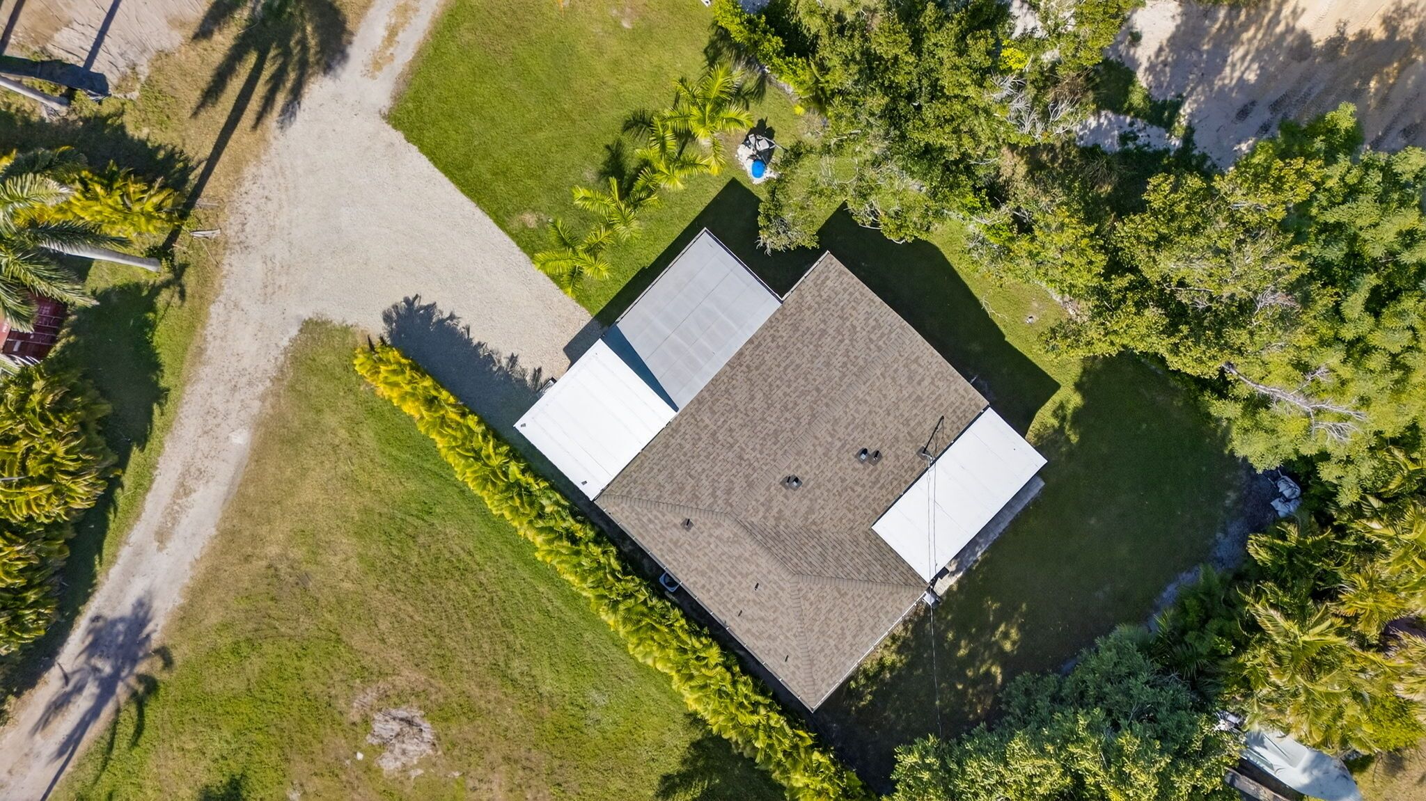 An aerial view of a building with a flat roof, surrounded by greenery and a paved area.