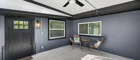 A room with a dark door, two windows with blinds, a ceiling fan, and a small round table with chairs.