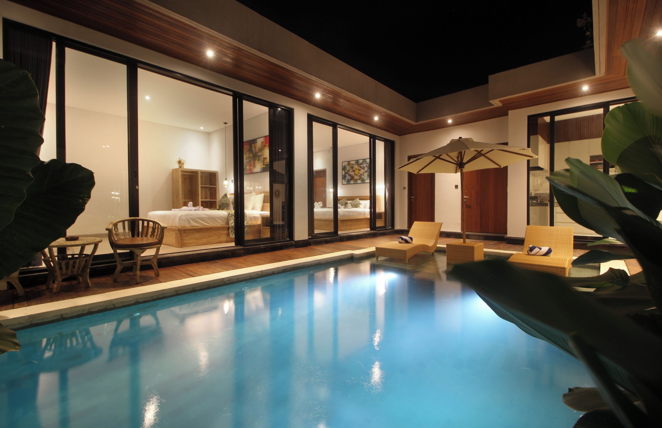 Ein moderner Poolbereich mit Glaswänden, einer Holzterrasse und Liegestühlen.