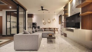 A modern living room with a grey sectional sofa, a coffee table, and a flat-screen TV mounted on a wooden wall.