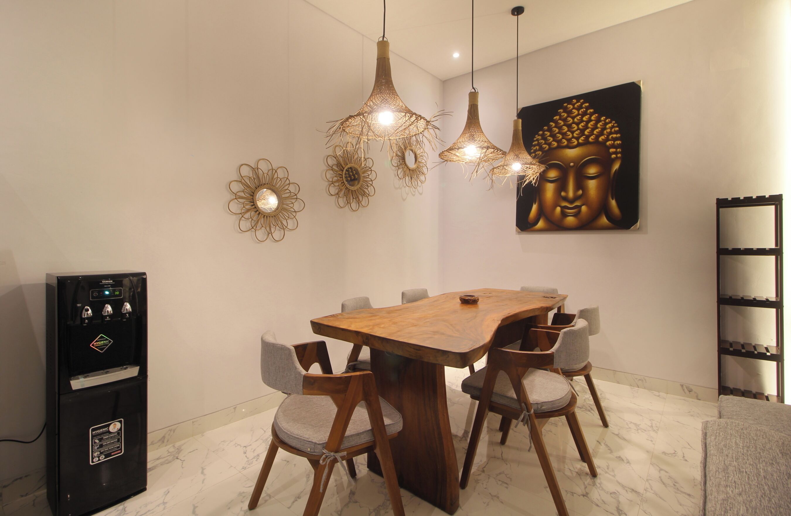 A dining area with a wooden table, six chairs, hanging pendant lights, wall art, and a refrigerator.