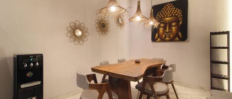 Un comedor con una mesa de madera, seis sillas, lámparas colgantes, decoración en la pared y un refrigerador.