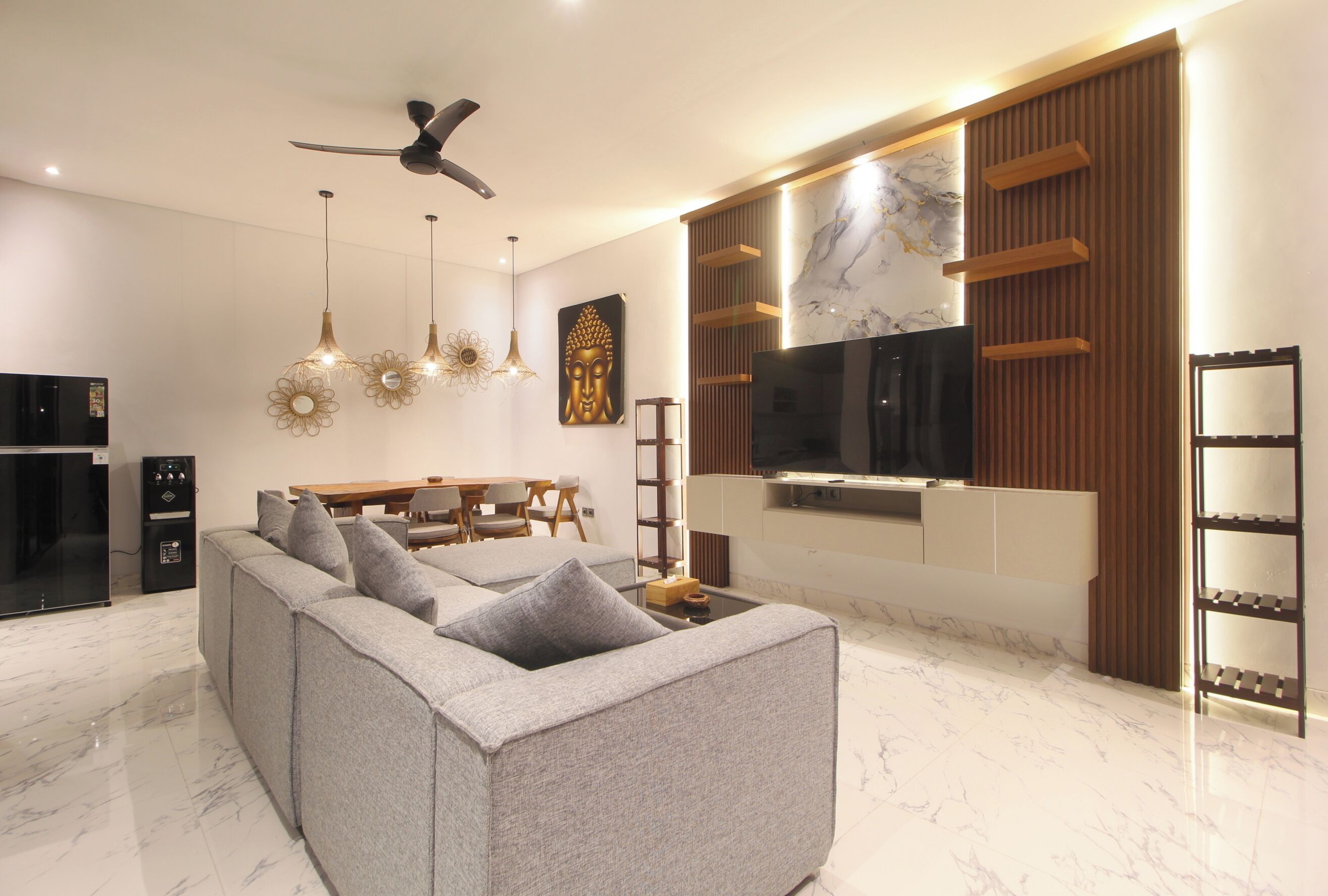Un salon moderne avec un canapé d’angle, un téléviseur à écran plat, un ventilateur de plafond, des luminaires suspendus et un sol en marbre.