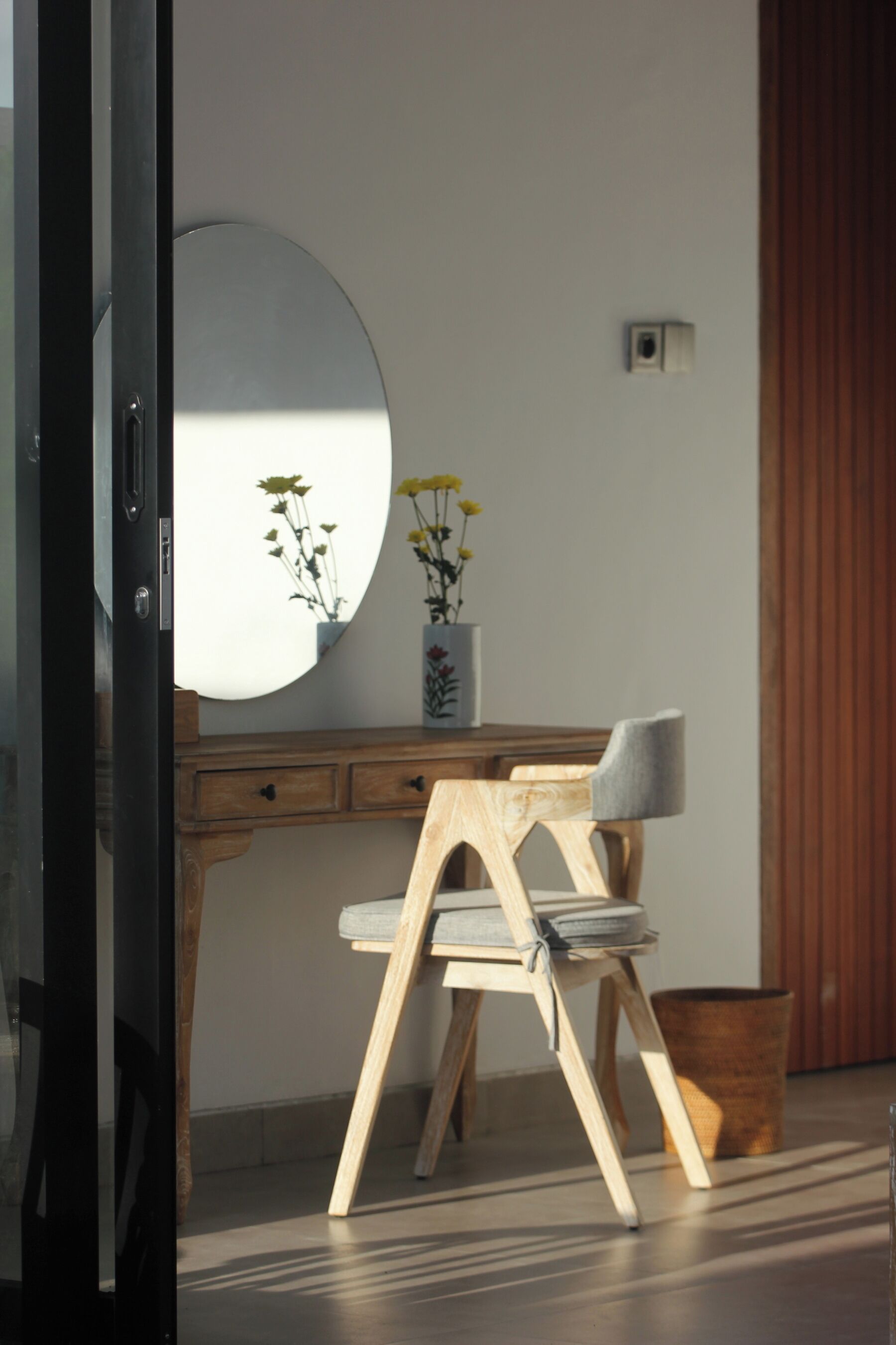 Una habitación con un escritorio de madera, una silla, un espejo y un florero con flores.