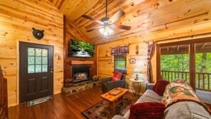 Ein Holzhäuschen im Inneren mit Kamin, Deckenventilator, Sofa und Blick ins Freie.