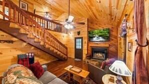 Ein rustikales Blockhaus-Interieur mit einer Holztreppe, einem Kamin, einem Fernseher und einem Sofa.