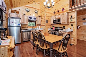A wooden cabin interior with a kitchen, dining area, and a chandelier.
