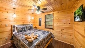 Ein Schlafzimmer einer Holzhütte mit einem Bett, einem Deckenventilator und einem Fenster.