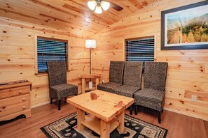 A cozy cabin interior with a wooden table, two chairs, a lamp, and a framed picture on the wall.