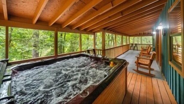 Eine Holzterrasse mit Whirlpool und Sitzgelegenheit, umgeben von Bäumen.