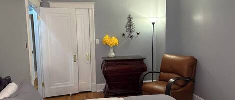 A bedroom with a bed, a dresser, a chair, a vase with flowers, and a lamp.