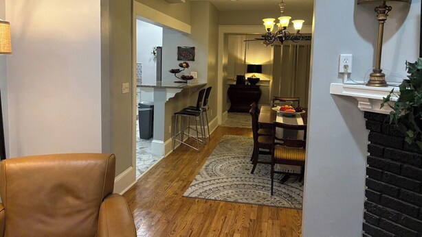 A hallway leading to a dining area with a table set for two, a chandelier, and a fireplace.