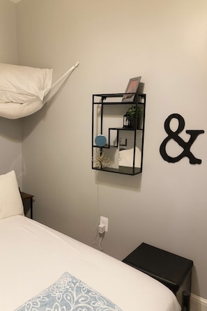 A bedroom with a bed, a bedside table, a wall-mounted shelf with decorative items, and a wall decoration. - DIAMOND CROWN LOFT - SUITE B (PHILADELPHIA)
