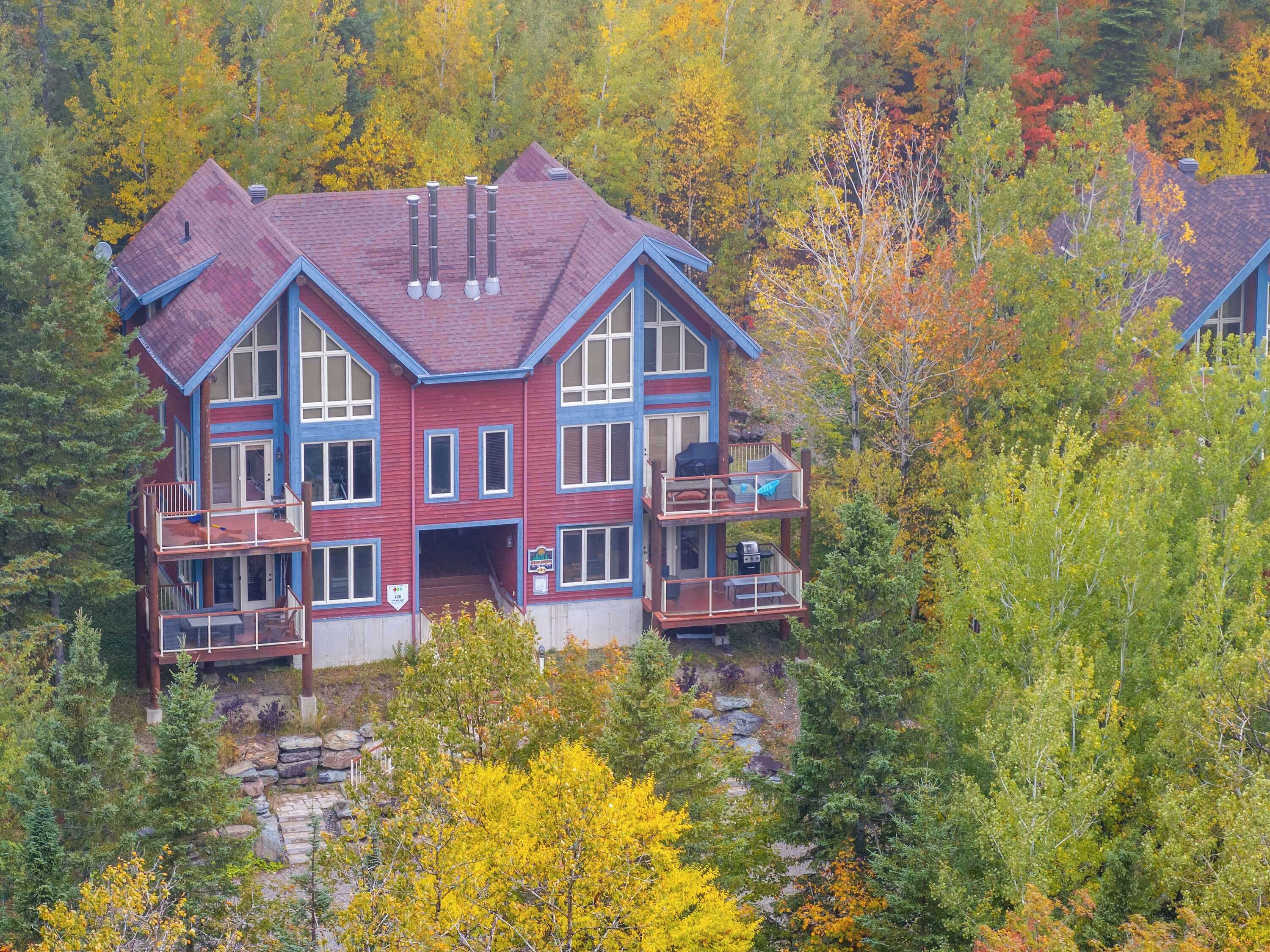 Une grande maison à plusieurs étages, à l’extérieur rouge et aux bordures bleues, entourée d’un feuillage automnal.
