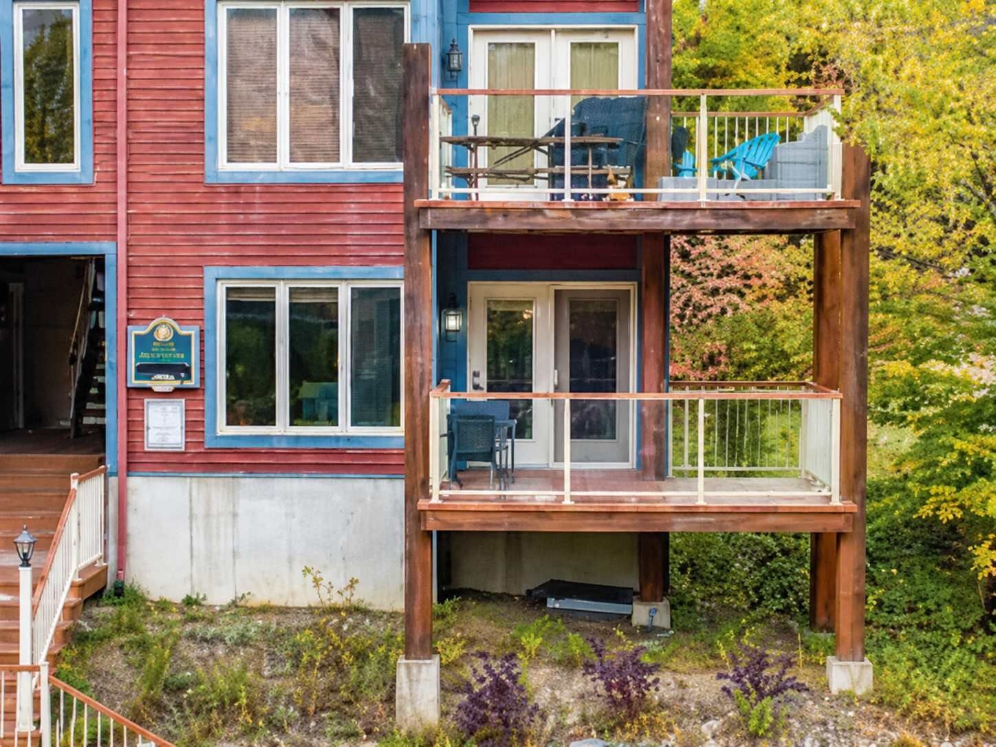 Un edificio de dos pisos con balcón, terraza de madera y un pequeño espacio para sentarse al aire libre.