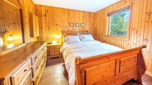 A wooden-paneled bedroom with a bed, dresser, and bedside lamps.
