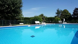 Ein klarer, blauer Pool mit gefliesten Rändern, umgeben von einem grünen Zaun und Bäumen.