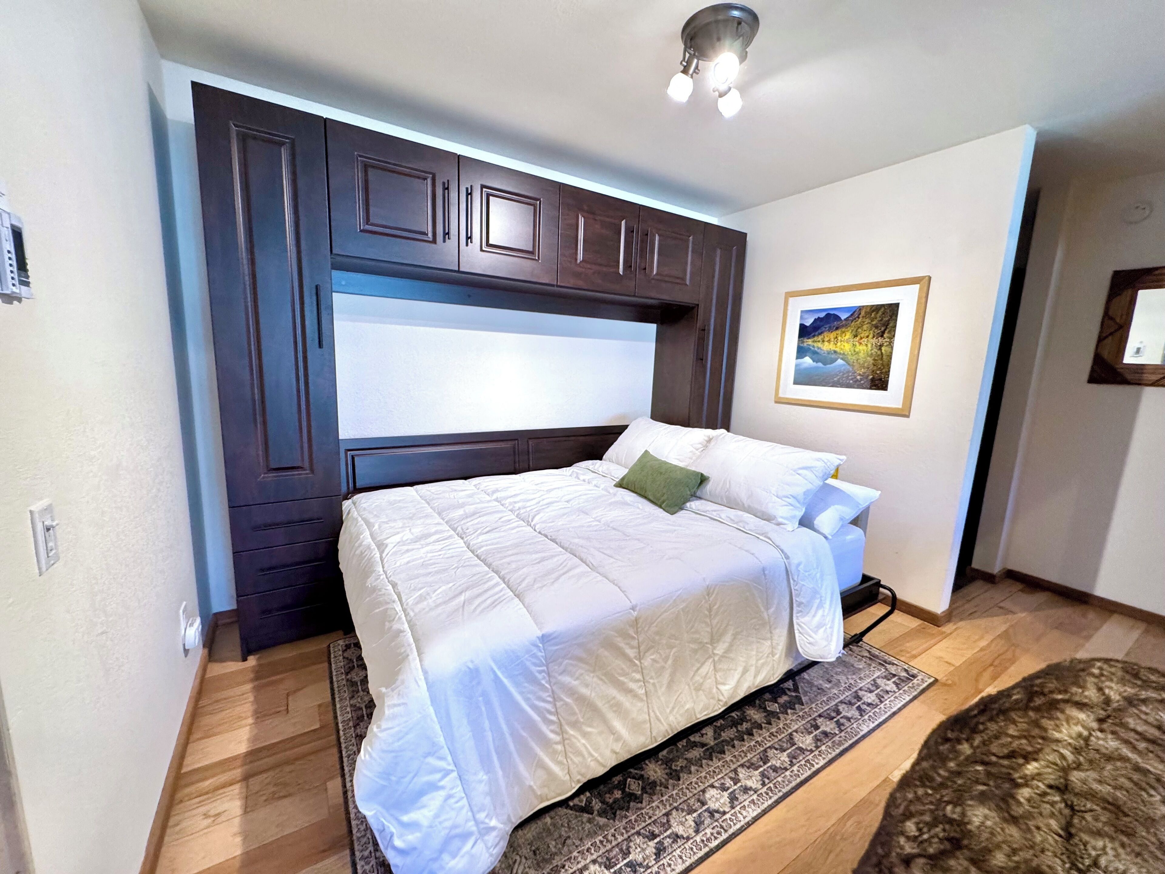 A bedroom with a large bed, dark wooden headboard, a framed picture on the wall, and a patterned rug.