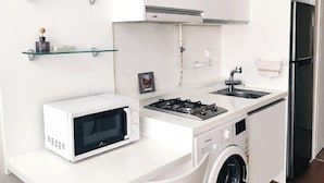 A compact kitchen with white cabinetry, a microwave, a stove, a sink, and a washing machine. There are two white chairs and glass shelves above the counter. - coex serena residence for business, travel, hospital (Seoul)