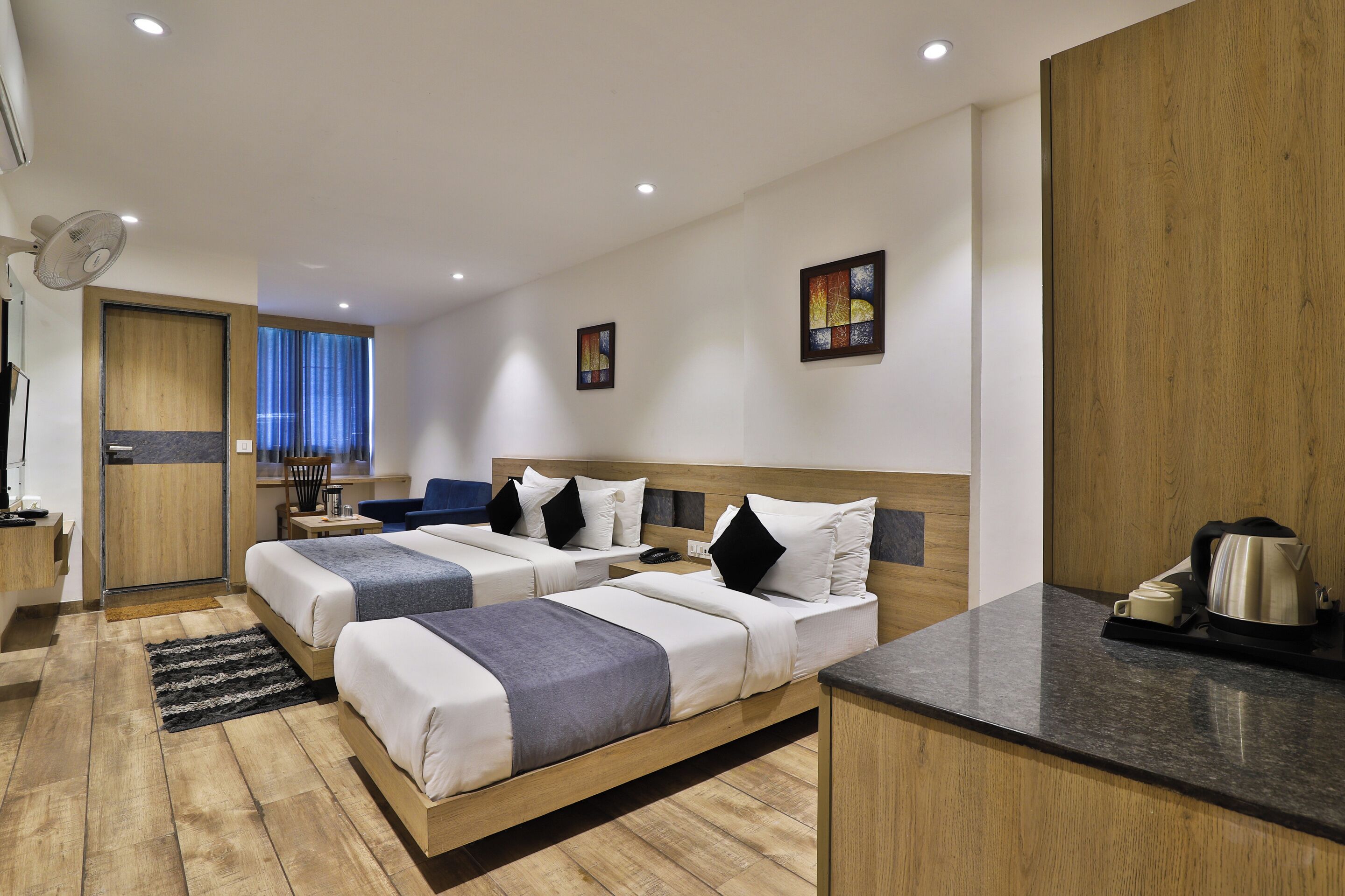 Een hotelkamer met twee bedden, een kitchenette, een houten vloer en een groot raam.