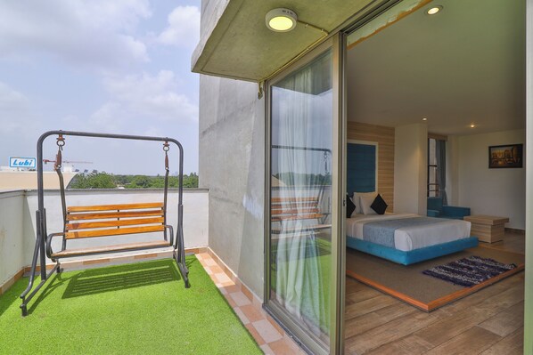 A balcony with a swing, a bed with blue bedding, and a view of the sky. - Hotel The Grand Shivay (Gandhinagar)
