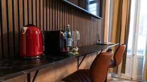 En köksbänk med en röd vattenkokare, en kaffemaskin, en flaska sprit och ett glas. Det finns två bruna stolar och ett fönster med gardiner.