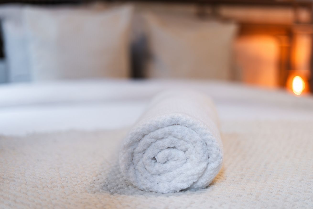 A neatly rolled white towel on a bed with a textured white cover.