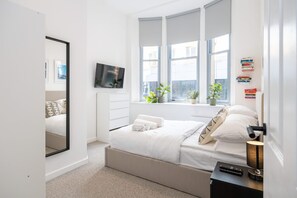 A modern bedroom with a large bed, a television, and a window with plants.