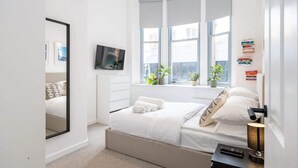 A modern bedroom with a large bed, a television, and a window with plants. - Azure Suite 1BR (Greater Manchester)