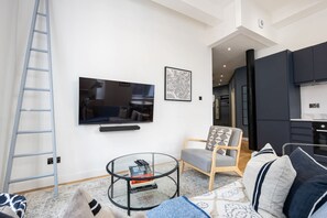 A modern living room with a TV, a glass coffee table, a sofa, a chair, and a kitchen in the background.
