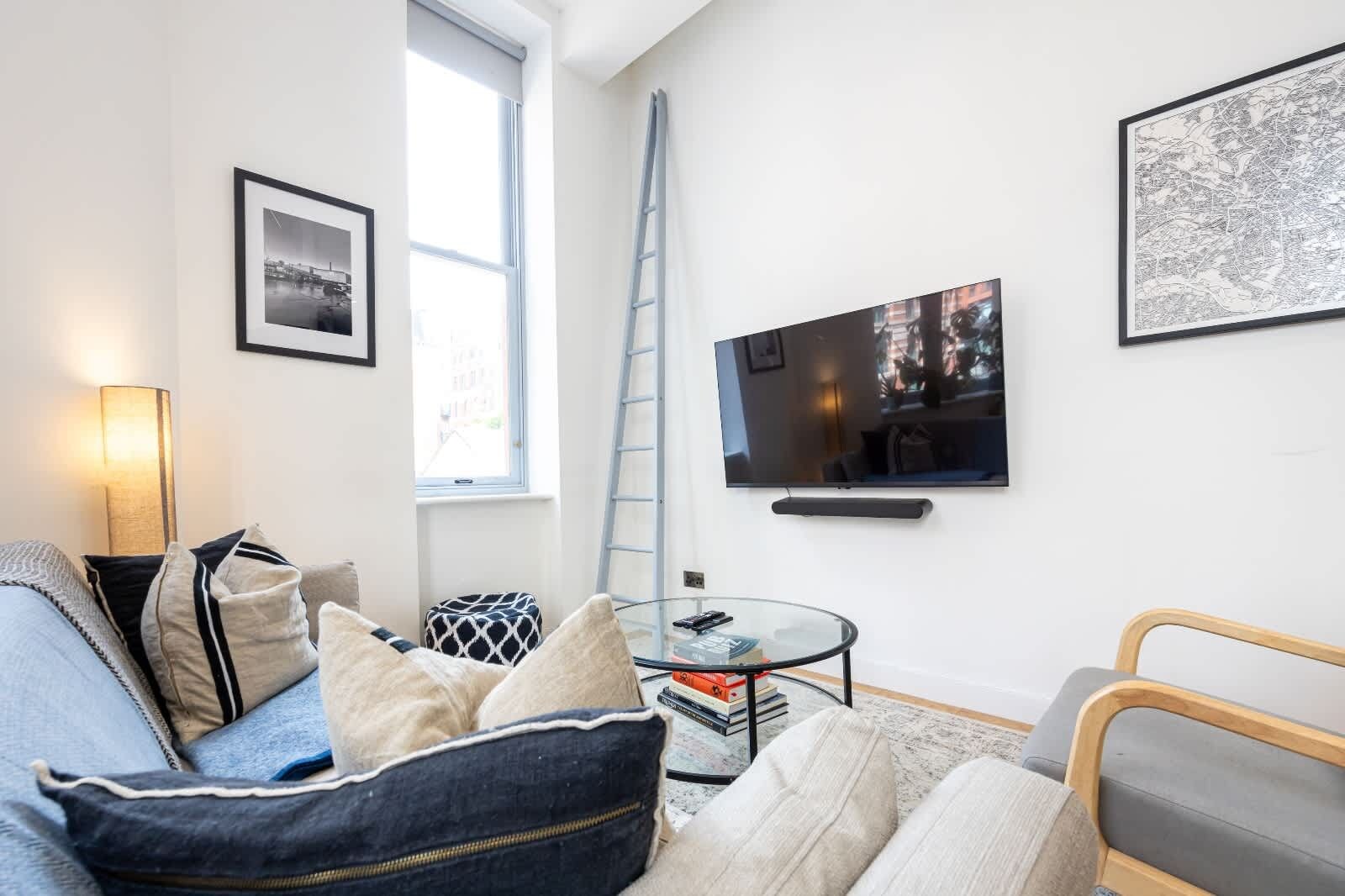 Una sala de estar moderna con un sofá, una mesa de centro, un televisor y una escalera apoyada en la pared.