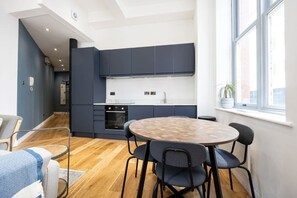 A modern kitchen with dark cabinets, a white countertop, and a built-in oven. There is a round wooden table with chairs in the foreground.