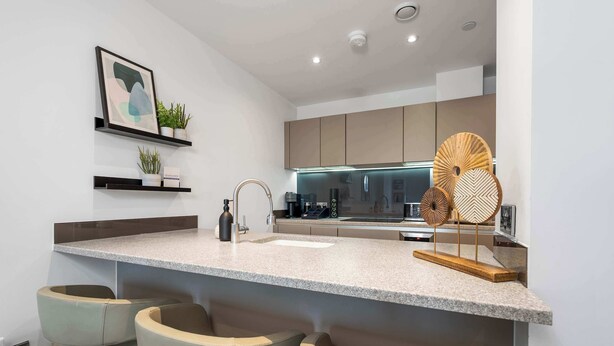 Eine moderne Küche mit einer Granitabdeckung, eingebauten Barhocker und einem hängenden Holzventilator.