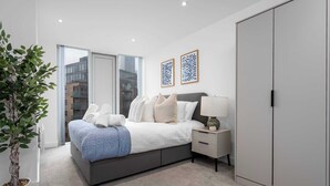 Ein modernes Schlafzimmer mit Bett, Nachttisch, Lampe, Kleiderschrank und einer Zimmerpflanze.