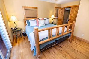 Una cama con estructura de madera y cabecera, dos mesitas de noche con lámparas, una ventana con persianas y un armario de madera.