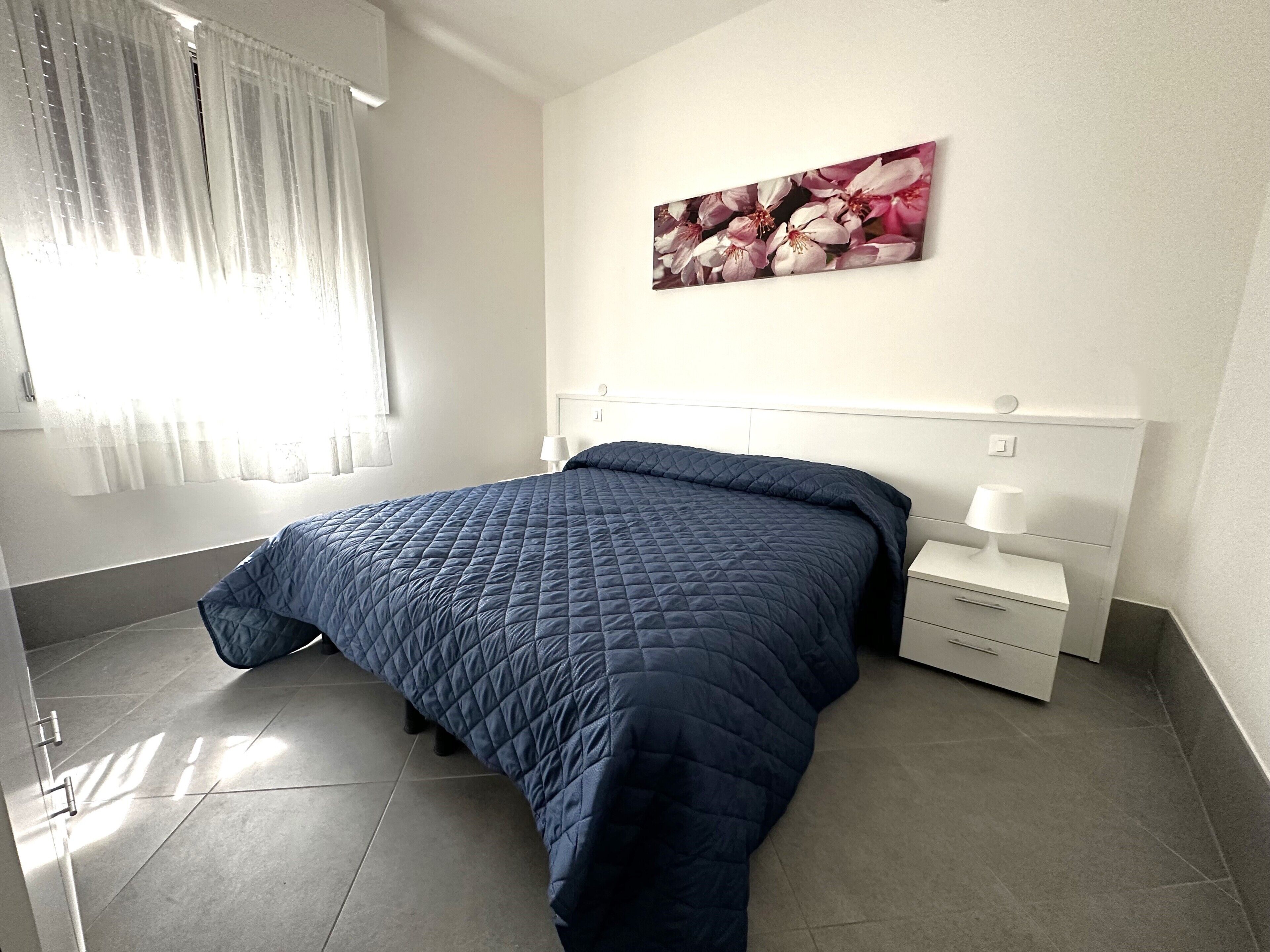 A bedroom with a bed, a nightstand, a lamp, and a window with curtains.