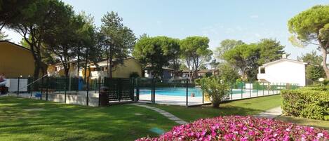 A residential area with a swimming pool, green lawns, and pink flowers.
