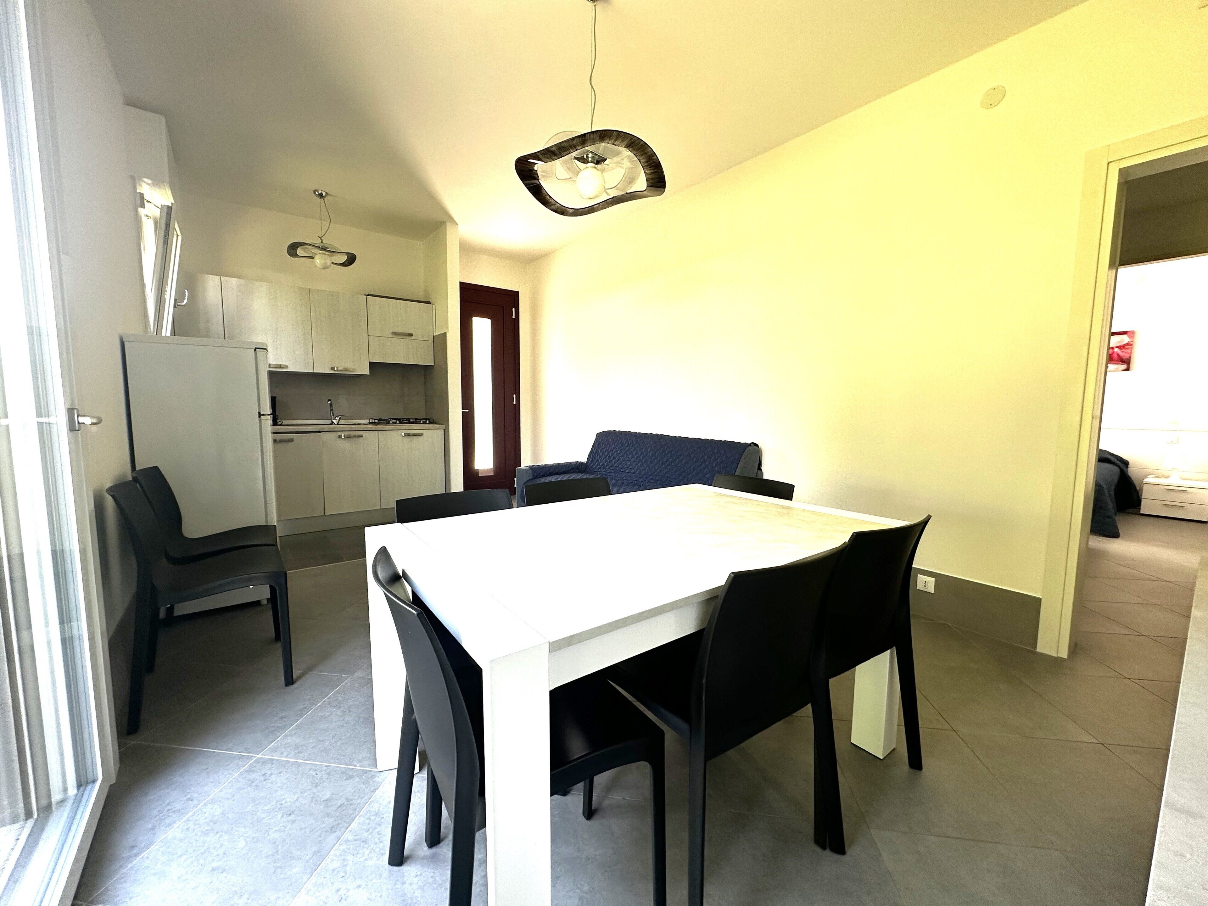 A compact kitchen with modern appliances and a dining area with a white table and black chairs.