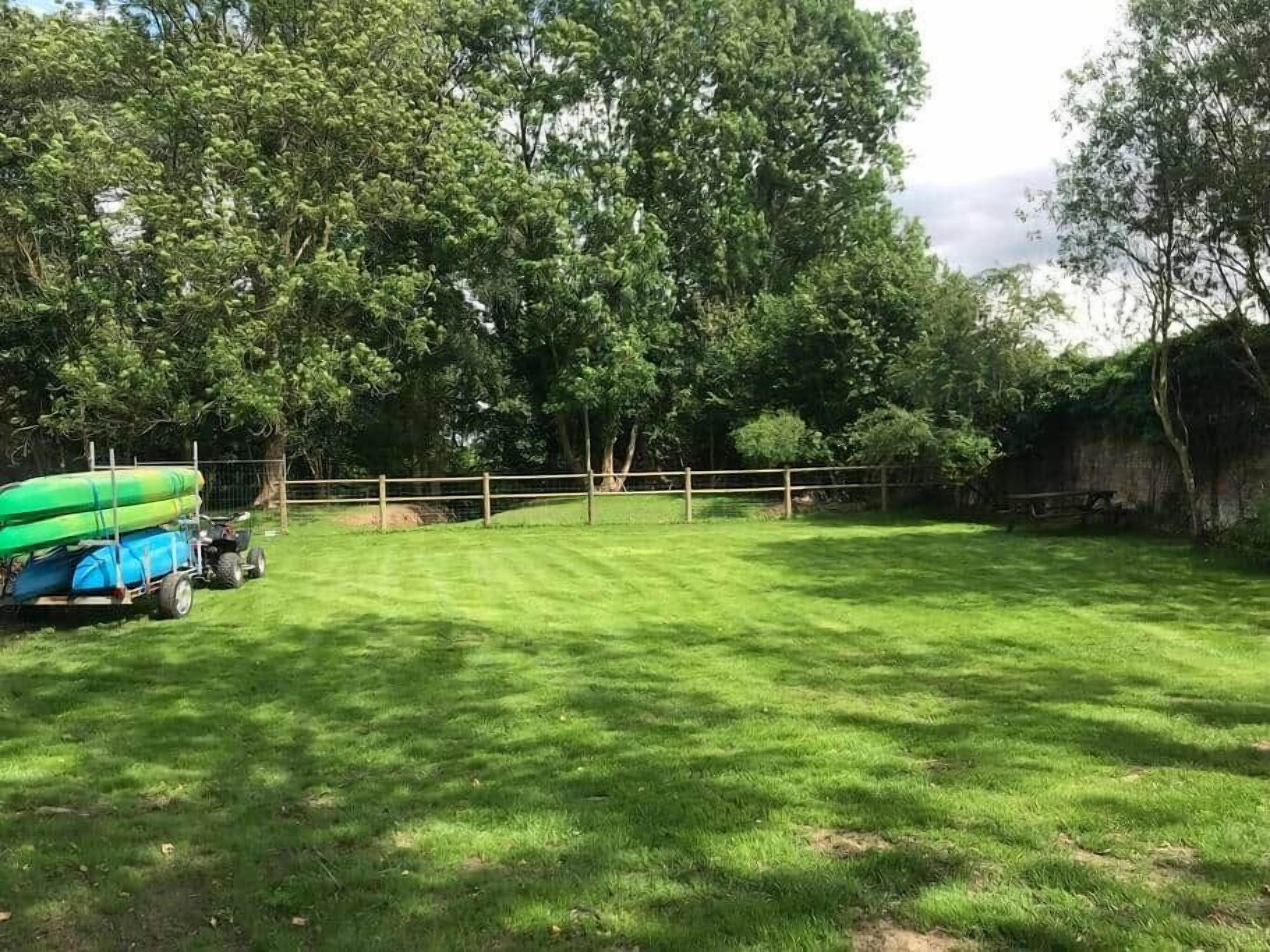 Un espace extérieur verdoyant, avec une clôture en bois, des arbres et un kayak vert posé sur une remorque.