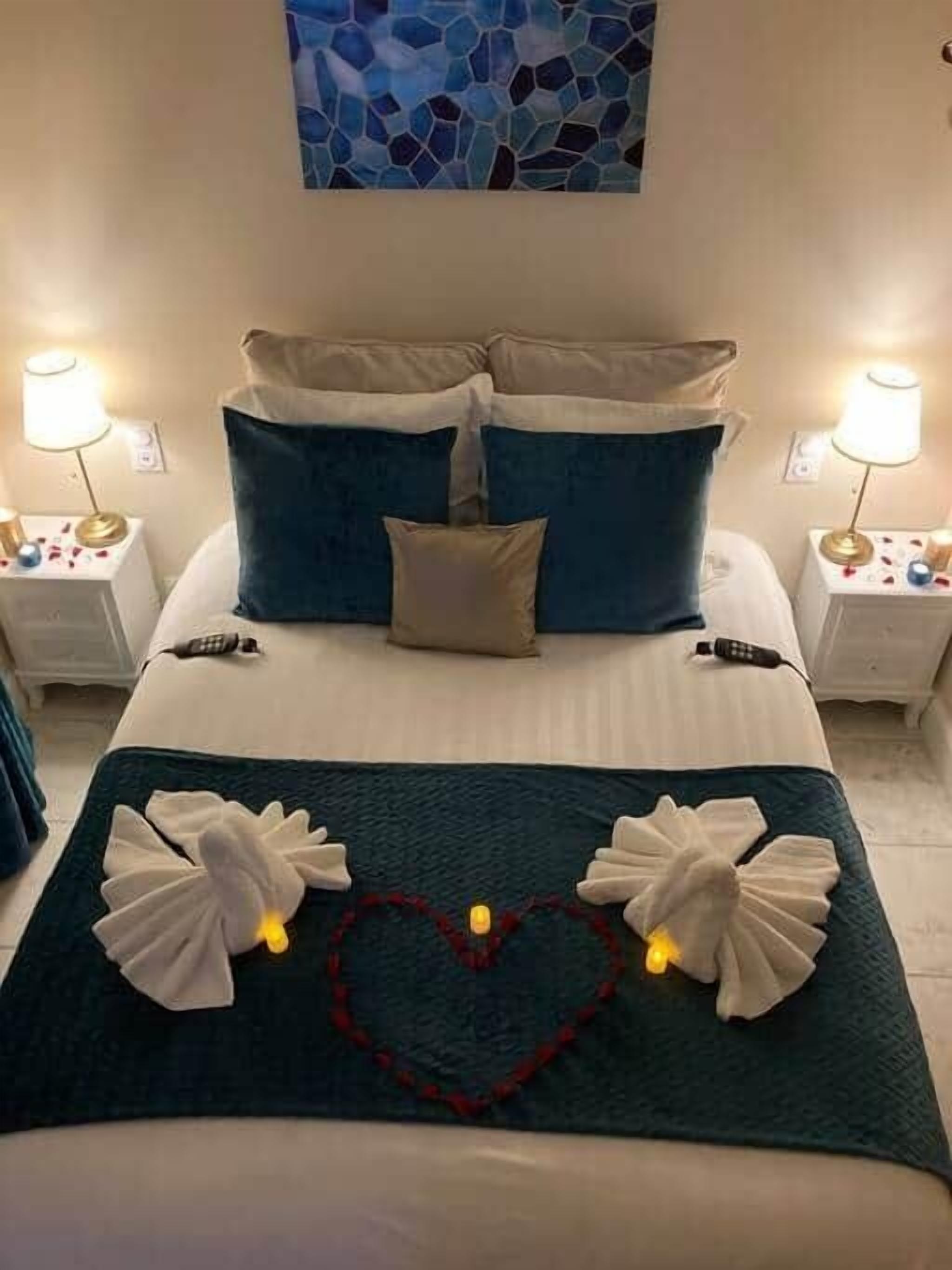A neatly made bed with a teal bedspread, two white towels, and a heart-shaped decoration on the bed.