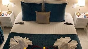 Een net opgemaakt bed met een blauwgroene sprei, twee witte handdoeken en een hartvormige decoratie op het bed.