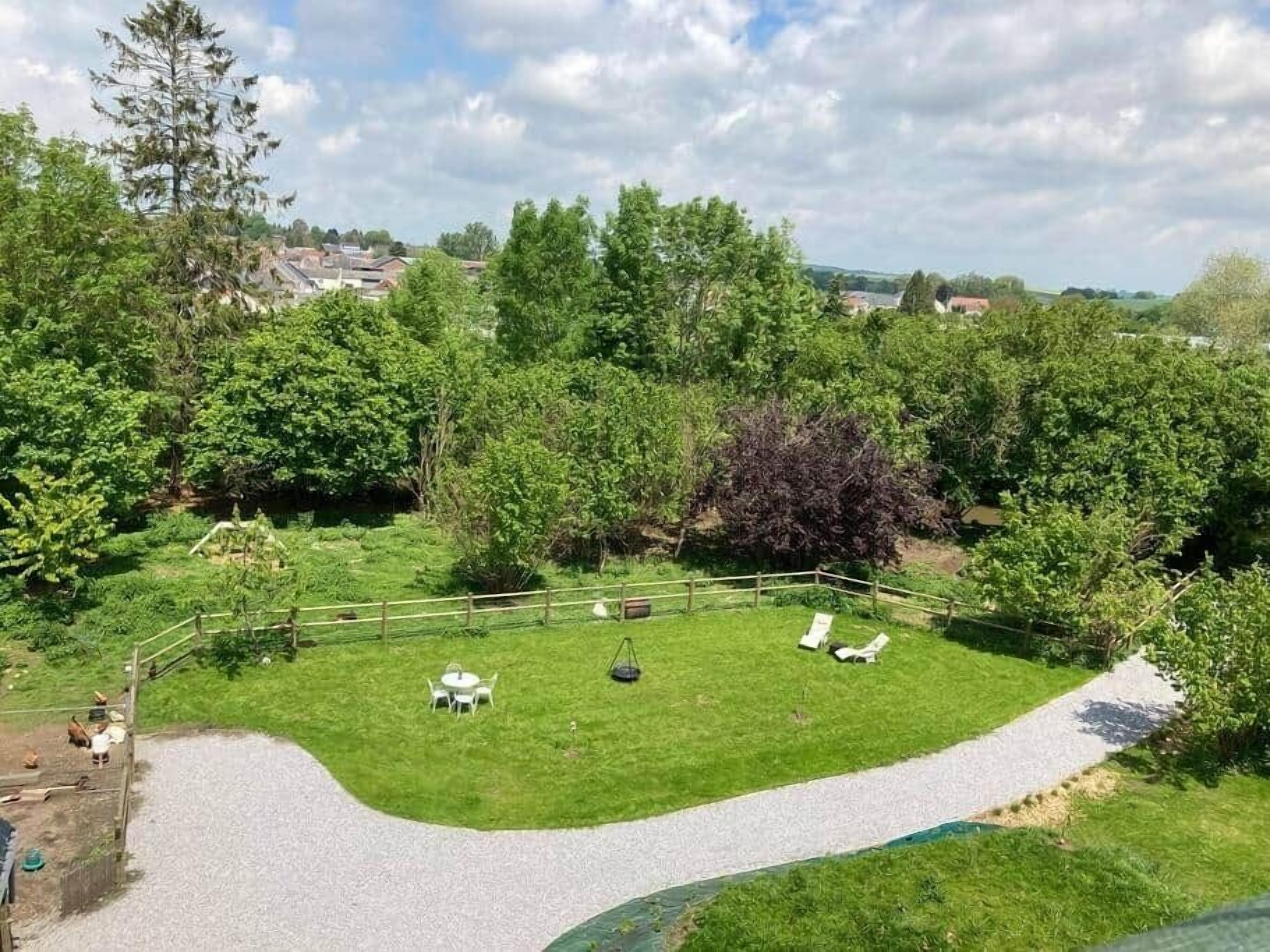 A grassy outdoor area with a curved gravel path, surrounded by trees and a wooden fence.