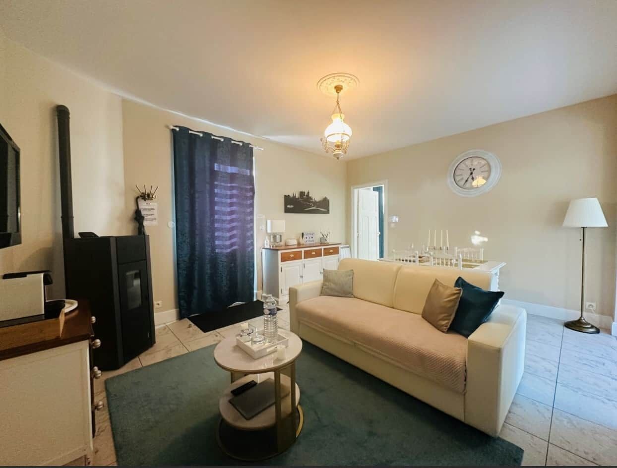 Een woonkamer met een bank, een salontafel, een lamp, een klok en een keuken op de achtergrond.