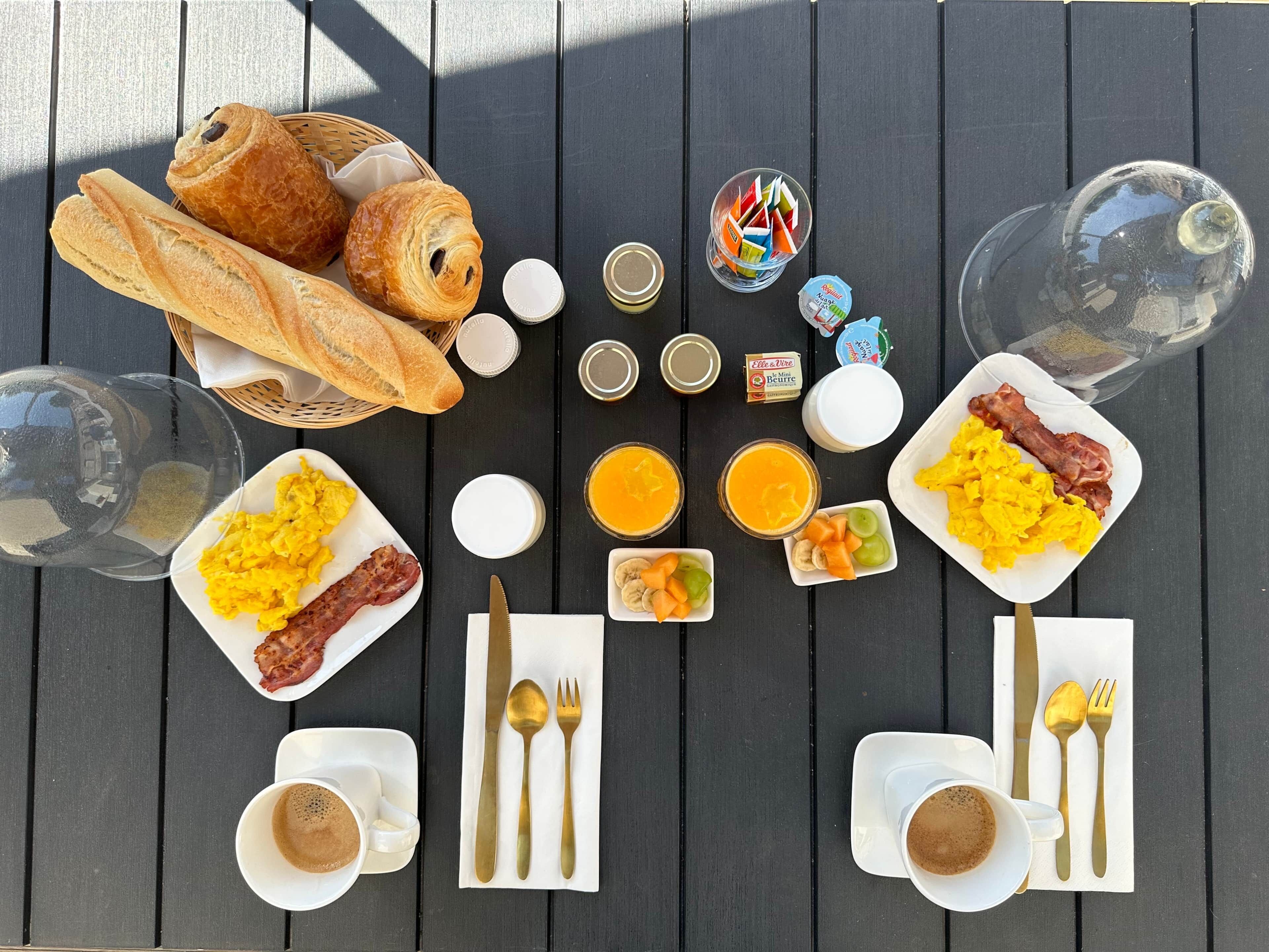 Taula de petit esmorzar amb croissants, ous remenats, bacon, fruita i cafè.