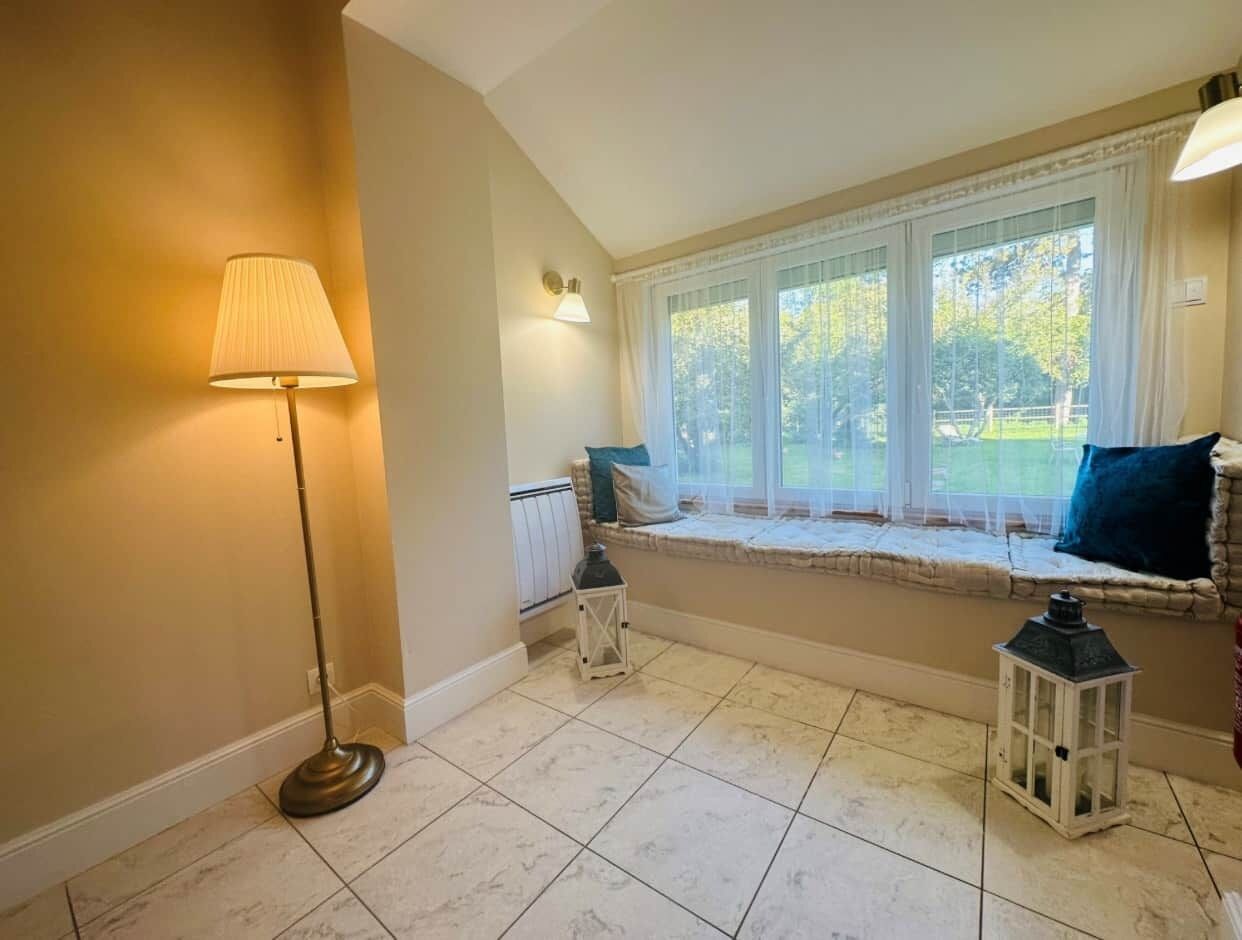 Una habitación con un asiento junto a la ventana, una lámpara de pie y dos faroles.