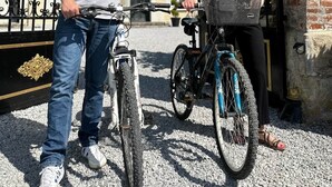 Ein Mann und eine Frau stehen vor einem schmiedeeisernen Tor, beide mit Fahrrädern.