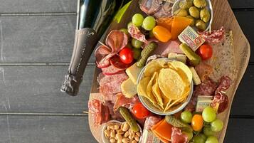 Una tabla de formatges i embutits variats, olives i pa sobre una taula de fusta, acompanyada d'una ampolla de vi i una cistella de pa.