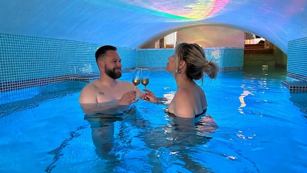 Ein Paar in einem Schwimmbecken mit gefliesten Innenwänden und einer gewölbten Decke.