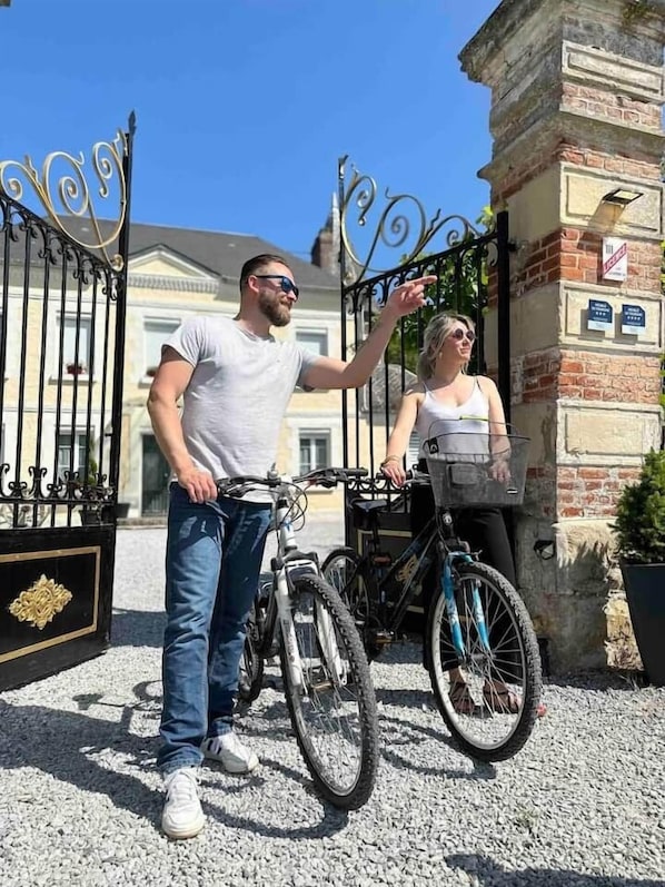 Un hombre y una mujer de pie frente a una entrada con puerta de reja y bicicletas.